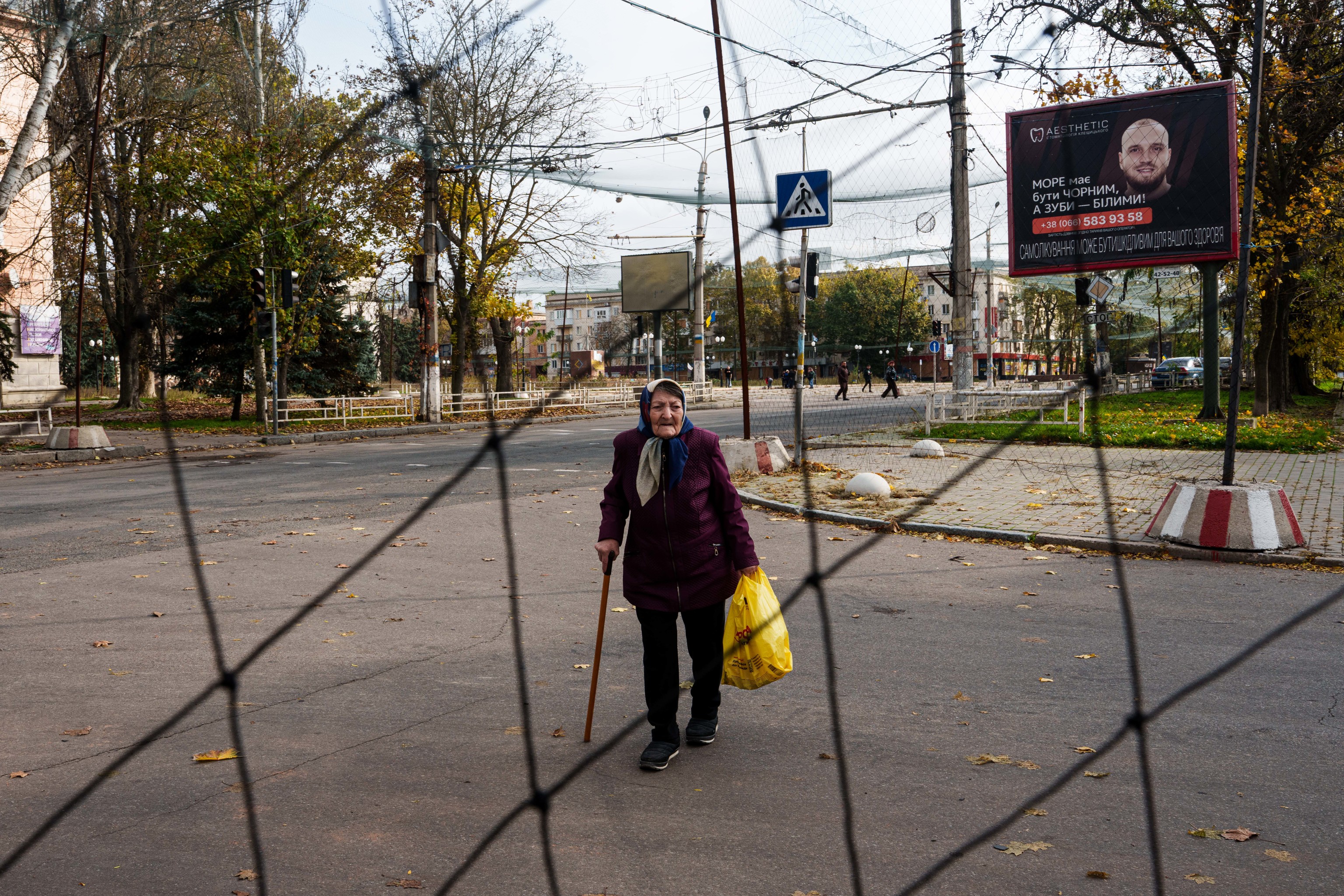 An elderly woman walks beneath anti-drone nets stretched over a street during a local ceasefire.